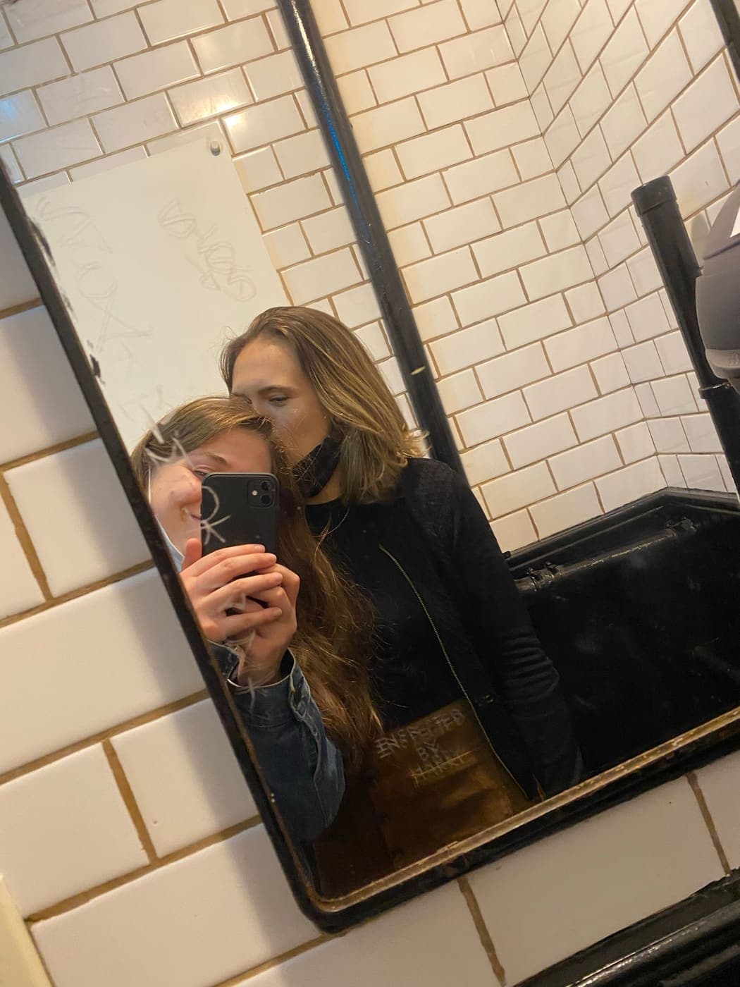 A mirror selfie in a tiled bathroom, one of us kissing the other on the cheek